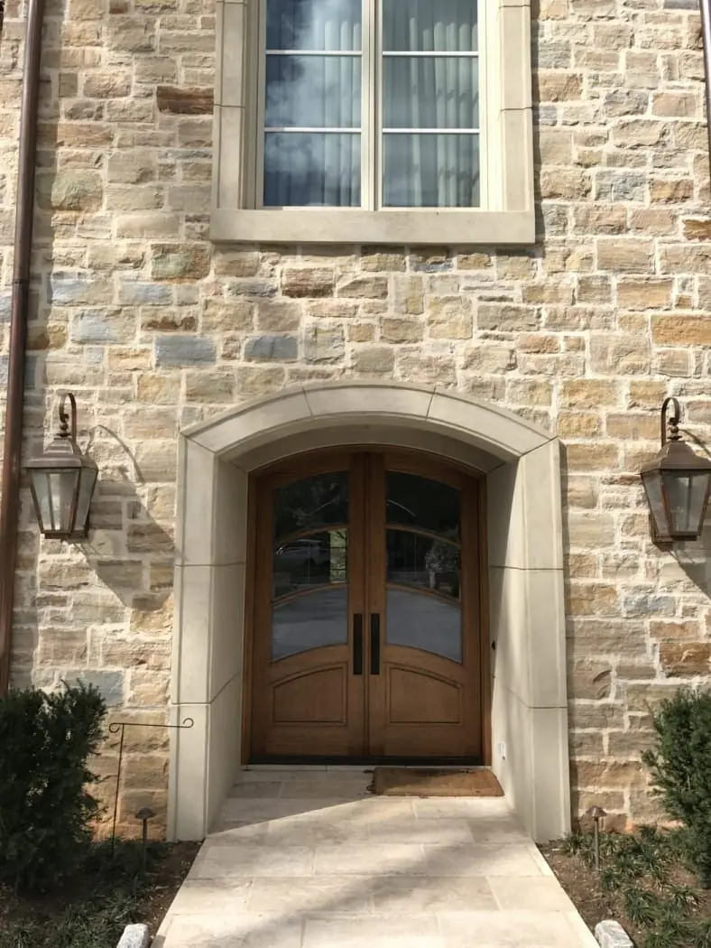 Arched cast-stone door surround set into a natural stone wall with copper lanterns