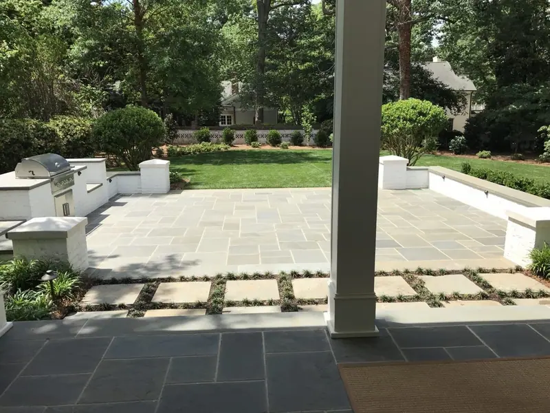 Bluestone porch opening onto a large patio with white stucco walls and a built-in grill
