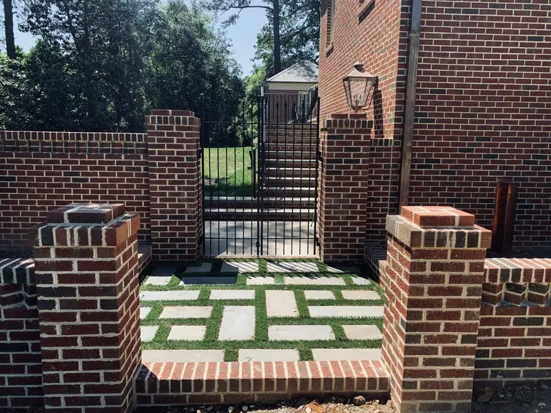 Brick piers and garden walls framing a bluestone-and-grass path to an iron gate