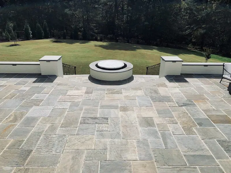 Round fire pit on a wide flagstone patio framed by a capped seat wall