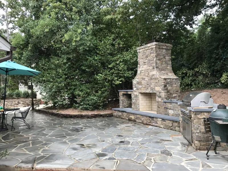 Stone outdoor fireplace, seat wall and built-in grill seen across a flagstone patio