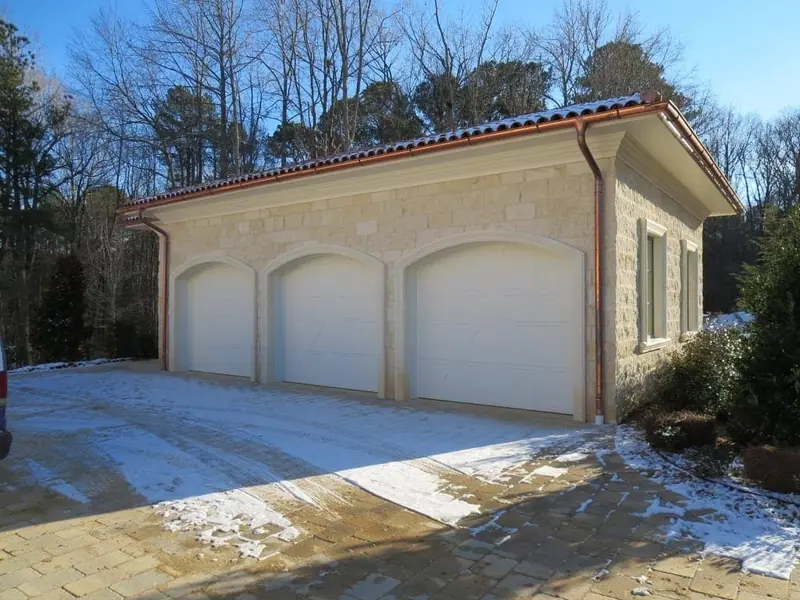 Three-bay garage clad in natural stone with arched door surrounds