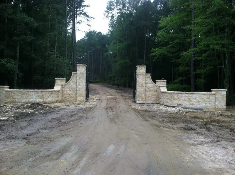 Limestone entry walls and piers flanking a wooded driveway