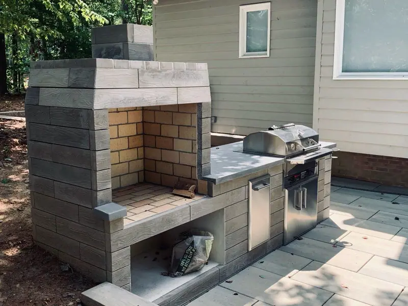 Outdoor kitchen and wood-burning fireplace in stacked stone block on a large-format paver patio