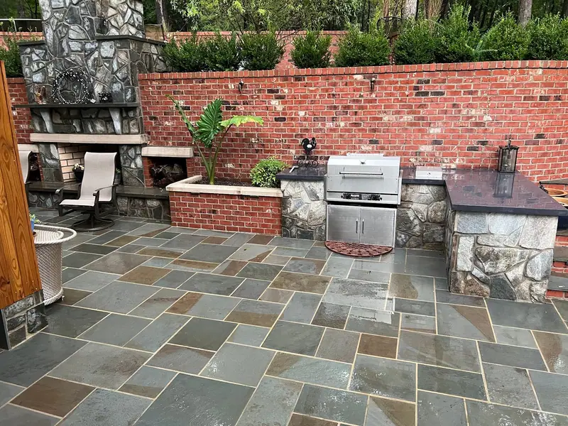 Outdoor kitchen with a stone fireplace, brick wall and bluestone patio