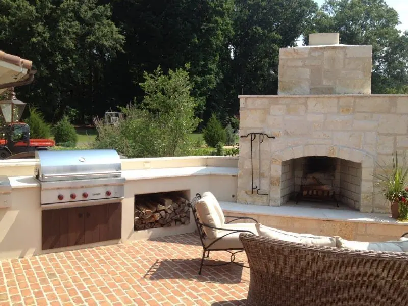 Limestone outdoor fireplace with a built-in grill beside a herringbone brick patio