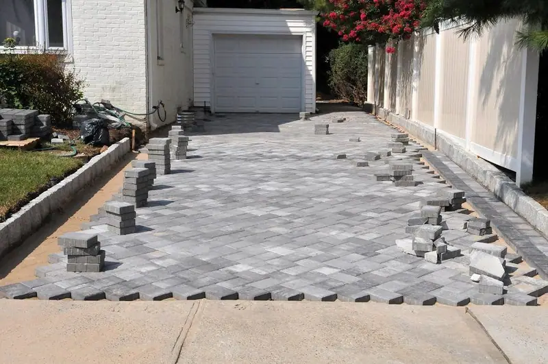 Paver driveway being laid course by course beside a garage