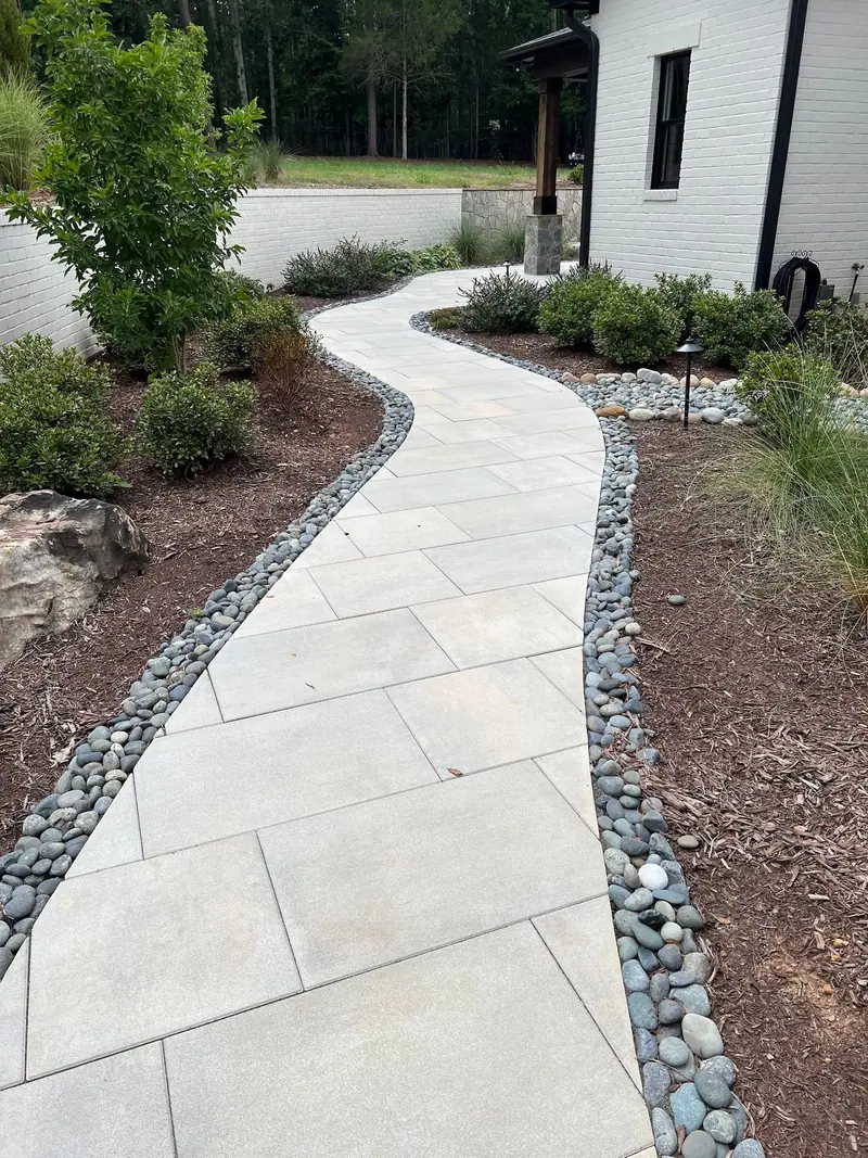 Large-format paver walkway edged with river rock beside a white brick house