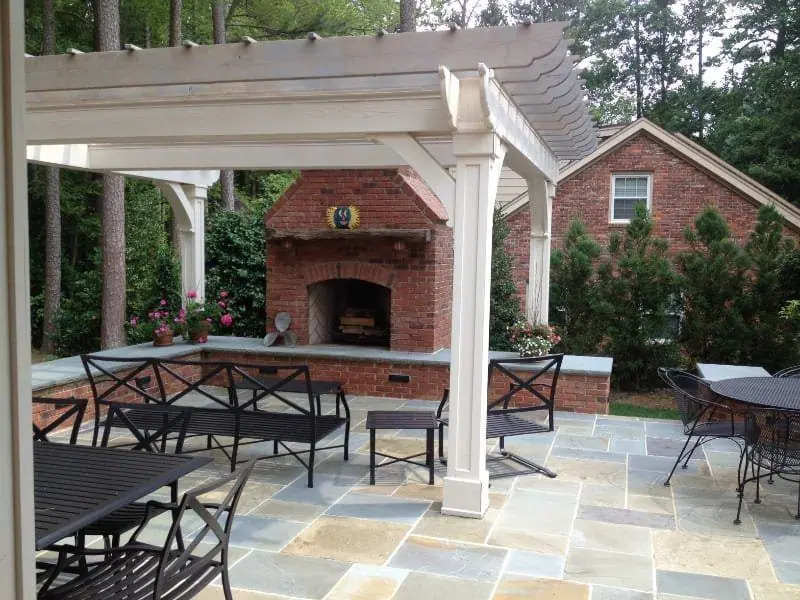 White pergola over a bluestone patio with a brick outdoor fireplace and counter