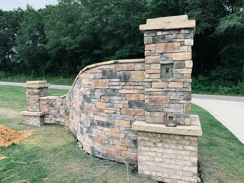 Sweeping stone entry wall with a capped pillar at a driveway