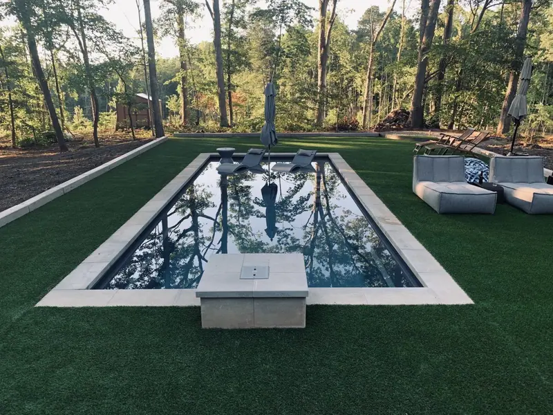 Artificial turf around a rectangular plunge pool in a wooded yard